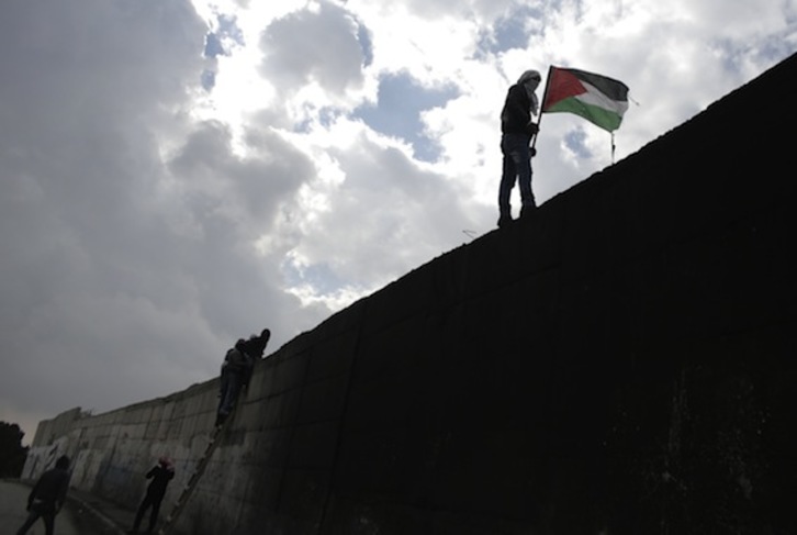Un hombre sostiene una bandera palestina sobre el muro del apartheid. (Ahmad GARABLI/AFP PHOTO