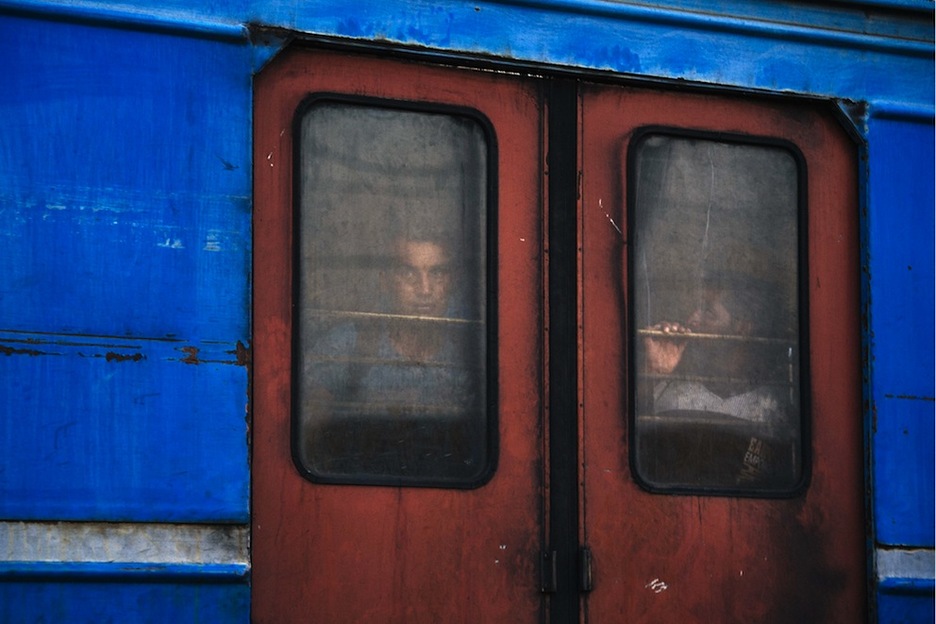 Dos refugiados miran a través de la ventana del tren que les trasladará a la frontera con Serbia. (Dimitar DILKOFF/AFP)