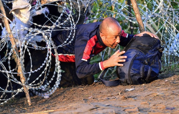 Un refugiado gatea por un alambrado en la frontera entre Hungria y Serbia, en Roszke. (Attila KISBENEDEK/AFP)