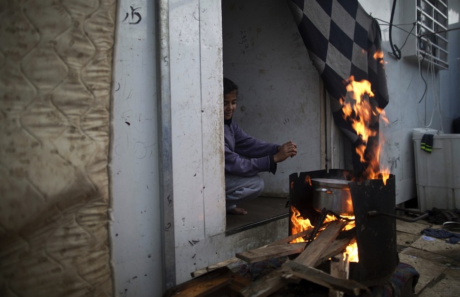 Una joven hace fuego en un bidón en la puerta de casa. (Mahmud HAMS / AFP)