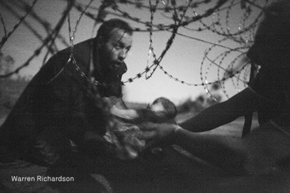 Un refugiado sostiene en brazos a un bebé en la valla entre Serbia y Hungría. Ganadora. (Warren RICHARDSON)