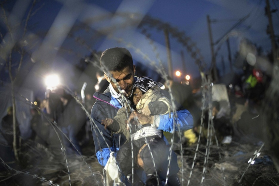 Un hombre con un bebé en brazos al otro lado de la valla. (ROBERT ATANASOVSKI / AFP)