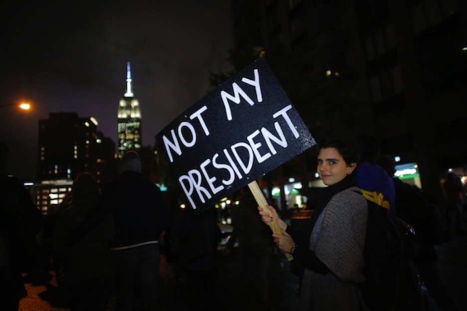 Una joven sostiene un cartel en el que dice, en referencia a Trump, que no es su presidente. (Kena BETANCUR/AFP)