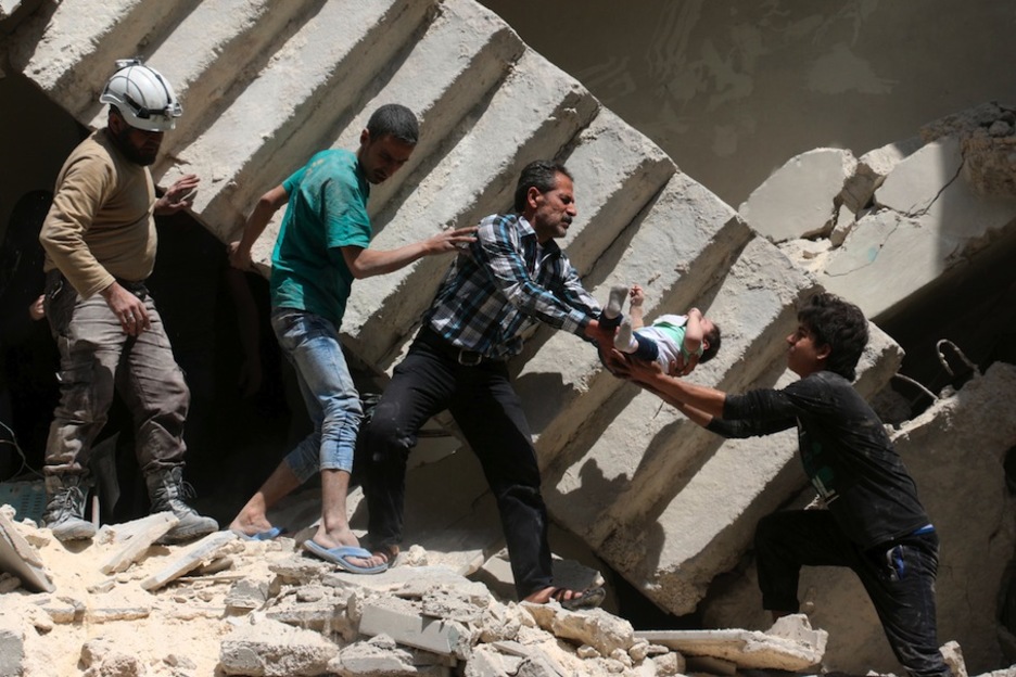 Voluntarios de defensa civil sirios rescatan a un bebé de los escombros de un edificio destruido tras un bombardeo. (Ameer ALHALBI/AFP)