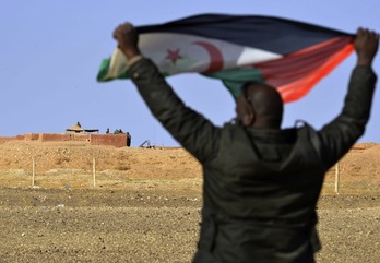 Un hombre agita la bandera saharui frente a unos soldados marroquíes que montan guardia. (Ryad KRAMDI/AFP)