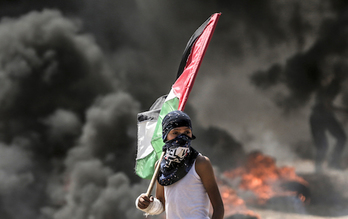 Un joven sujeta la bandera palestina frente al humo de los neumáticos quemados. (Mahmud HAMS / AFP)