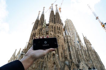 Un dispositivo muestra la app de Uber junto a la Sagrada Familia de Barceloan. (Josep LAGO/AFP)