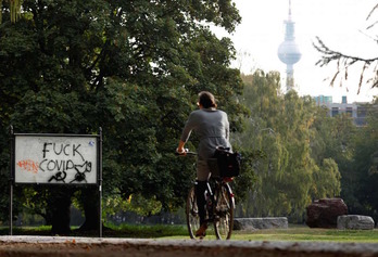 Una ciclista pasa junto a un cartel que maldice el covid en Berlín. (Odd ANDERSEN/AFP)