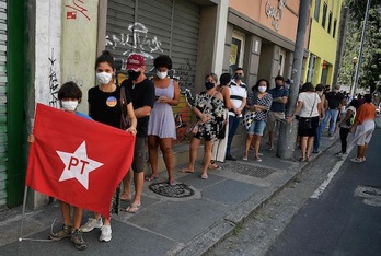 Un joven agarra una bandera con el logotipo del PT mientras la gente espera para votar en Río de Janeiro. (Carlos DE SOUZA/AFP)