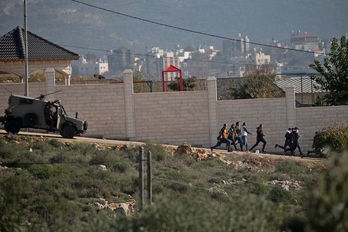 Jóvenes palestinos corren ante un vehículo del Ejército israelí en una protesta contra la construcción de colonias en Cisjordania. (Jaafar ASHTIYEH/AFP)