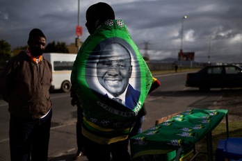 Un hombre envuelto en un gran pañuelo con una foto del presidente de Sudáfrica y líder del ANC, Cyril Ramaphosa, frente a un colegio electoral el pasado lunes. (Rodger BOSCH/AFP)