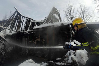 Un bombero rocía agua sobre las casas calcinadas que están cubiertas de nieve. 
