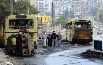 Civiles sirios pasan junto a vehículos calcinados en Alepo. (Philippe DESMAZES/AFP PHOTO)