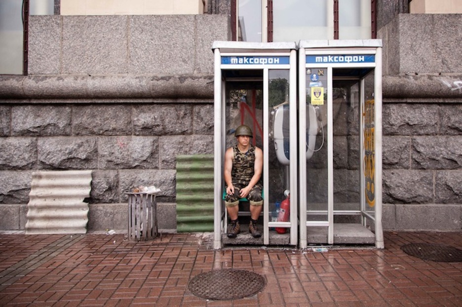 Miembro de autodefensa del Maidán se resguarda de la lluvia en una cabina telefónica. (Juan TEIXEIRA)
