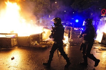 Dos policías pasan ante unos contenedores en llamas. (Josep LAGO/AFP PHOTO)