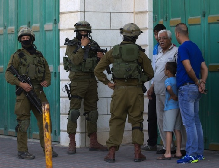 Soldados israelíes preguntan a varios palestinos, en las calles de Hebrón. (Menahem KAHANA/AFP PHOTO)