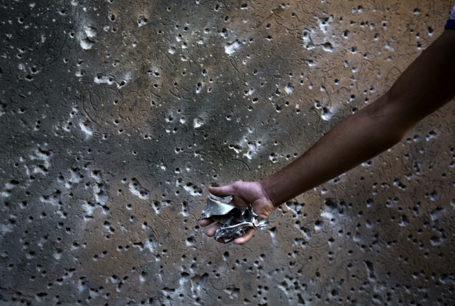 Un hombre sujeta restos de misiles ante una pared ametrallada. (Mohammed ABED/AFP)