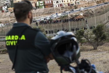 Un guardia civil vigila la frontera de Melilla mientras decenas de migrantes aguardan hasta el agotamiento. (José COLÓN / AFP)