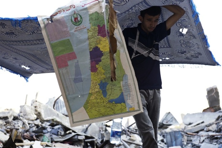 Un palestino porta objetos que ha podido recuperar de una vivienda en Gaza. (Roberto SCHMIDT / AFP)
