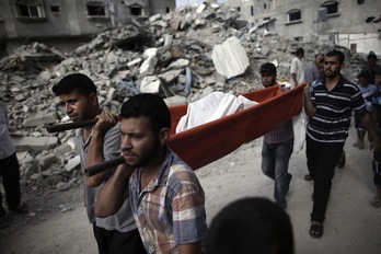 Cuatro hombres llevan a uno de los fallecidos durante los bombardeos de ayer. (THOMAS COEX / AFP) 