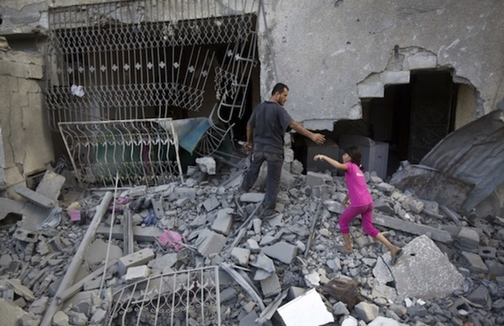 Dos personas caminan sobre los escombros de un edificio bombardeado por Israel en Gaza. (Mahmud HAMS/AFP PHOTO)