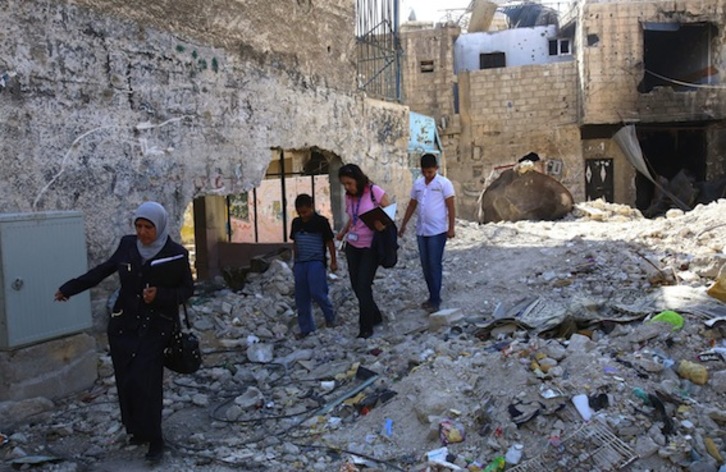 Una profesora de la UNRWA camina entre los escombros de Gaza junto a dos niños palestinos. (Yousseff KARWASHAN/AFP PHOTO)