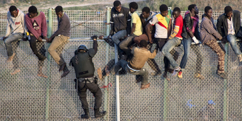 Un guardia civil trata de alcanzar a varios subsaharianos encaramados en la valla de Melilla (AFP)