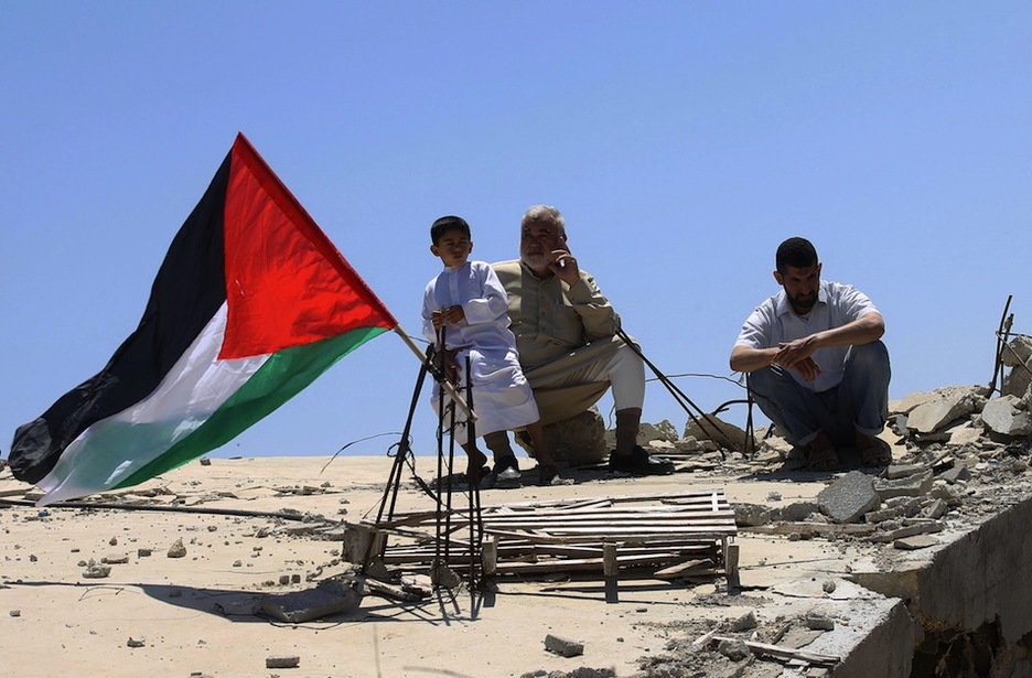 Un menor con una bandera palestina junto a una casa derruida en Gaza. (Said KHATIB / AFP)Sai