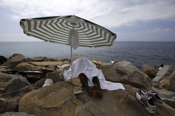 Un migrante duerme bajo una sombrilla en las costas italianas. (Valery HACHE/AFP PHOTO)