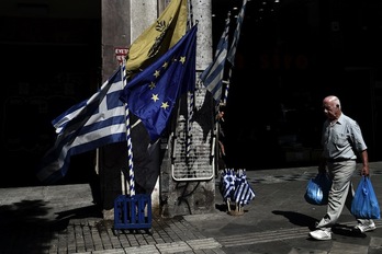 Un hombre camina por Atenas junto a banderas griegas y una europea. (Aris MESSINIS / AFP)
