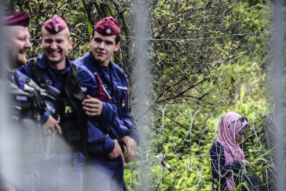 Policías húngaros relajados, con una mujer al otro lado de la alambrada fronteriza. (Armend NIMANI / AFP)