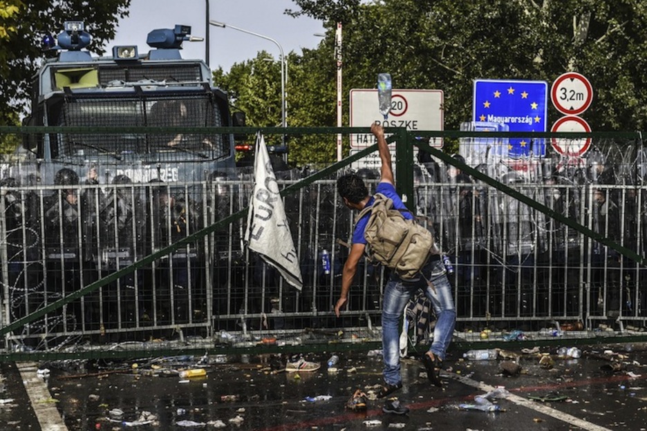Un refugiado arroja una botella de plástico por encima de la verja fronteriza. (Armend NIMANI / AFP) Un refugiado arroja una botella de plástico por encima de la verja fronteriza. (Armend NIMANI / AFP)