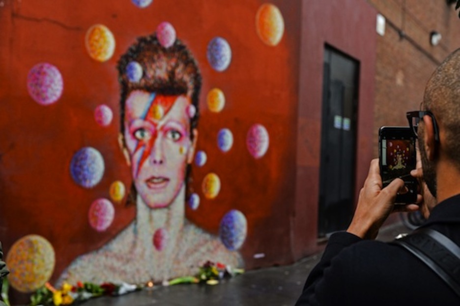 Un hombre fotografía un mural de Bowie en Londres, con flores en su memoria. (Chris RATCLIFFE/AFP) 