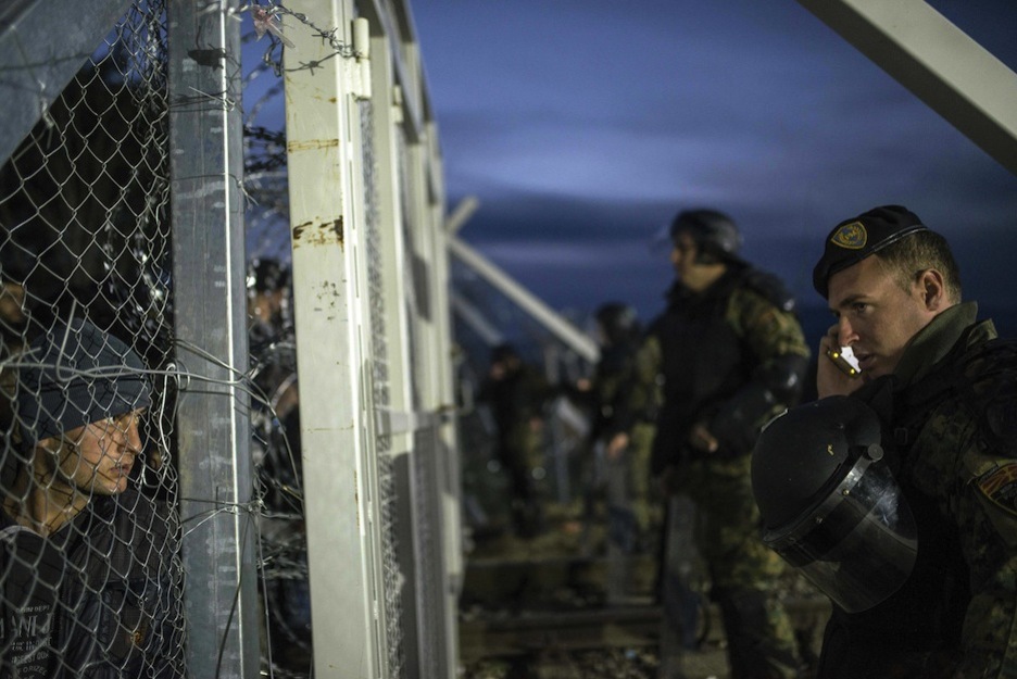 Un agente macedonio habla por teléfono observado por un refugiado. (ROBERT ATANASOVSKI / AFP)