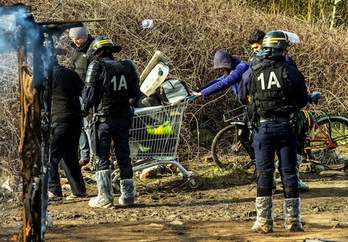 Policías antidisturbios observan a varias personas que trasladan sus pertencias en el campamento de Calais. (Philippe HUGUEN/AFP)