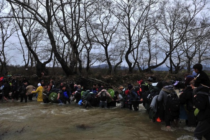Un grupo de refugiados traspasa la frontera entre Grecia y Macedonia cruzando un río. (Sakis MITROLIDIS/AFP)
