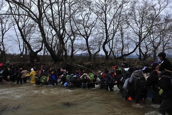Un grupo de refugiados traspasa la frontera entre Grecia y Macedonia cruzando un río. (Sakis MITROLIDIS/AFP)