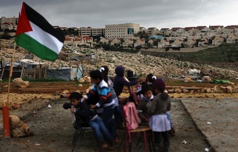 Un grupo de niños palestinos toma clase, con la colonia de Maale Adumin de fondo. (Ahmad GHARABLI/AFP)