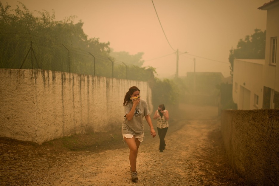 Dos mujeres se cubren la boca y la nariz con un pañuelo para no inhalar humo en la localidad de Torgal. (Patricia DE MELO/AFP)
