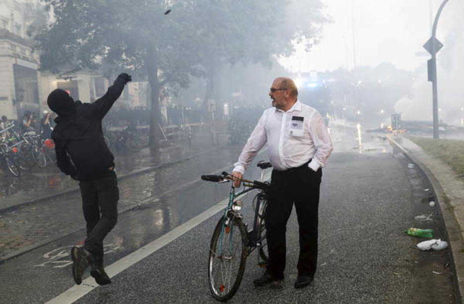 Hamburgo, día 7 de julio. Un ciclista contempla cómo un manifestante lanza una piedra durante las protestas por la cumbre del G20. (Odd ANDERSEN)