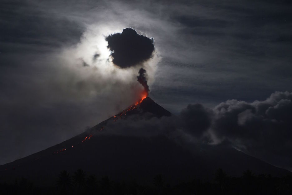 La "súper luna de sangre azul" oscurecida por las nubes ilumina el volcán Mayon. AFP PHOTO / TED ALJIBE  
