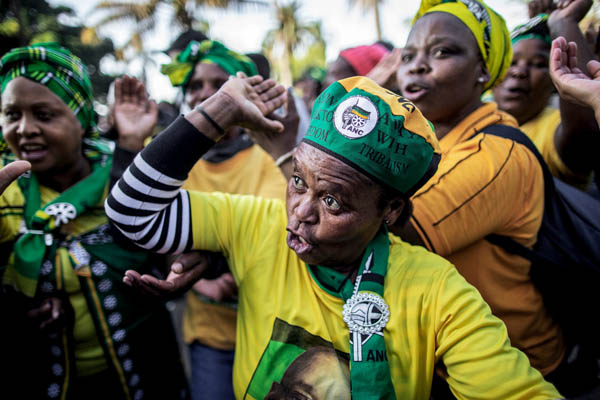 Un grupo de personas vestidas con los colores del Congreso Nacional Africano cantan y bailan a las puertas del Tribunal Supremo durante una manifestación en apoyo del ex presidente Jacob Zuma.