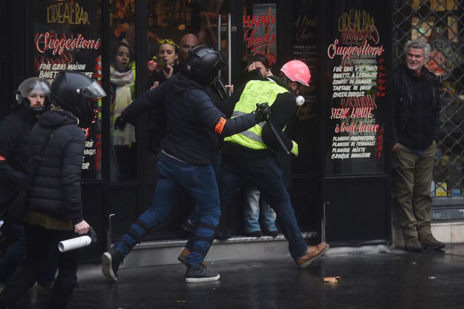 Kalez jantzitako polizia bat, manifestari bat kolpatzen. Lucas BARIOULET/AFP)