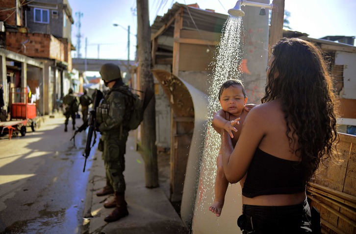 Una mujer baña a su hijo ante una patrulla militar en la favela de Manguinhos. (Carl SOUZA / AFP)
