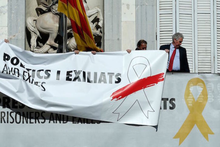 Operarios cuelgan una pancarta con un lazo blanco en el edificio de la Generalitat. (Pau BARRENA/AFP)