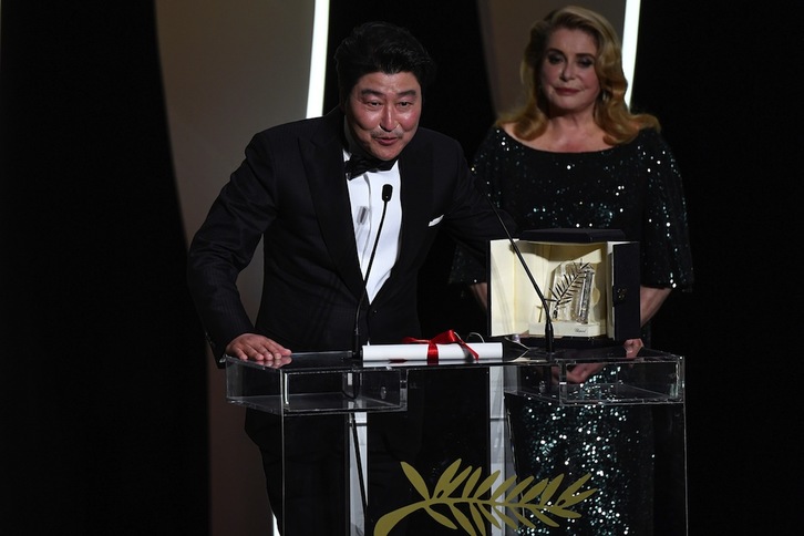 Bong Joon-ho se dirige al público tras recibir la Palma de Oro, bajo la atenta mirada de Catherine Deneuve. (Christophe SIMON/AFP)