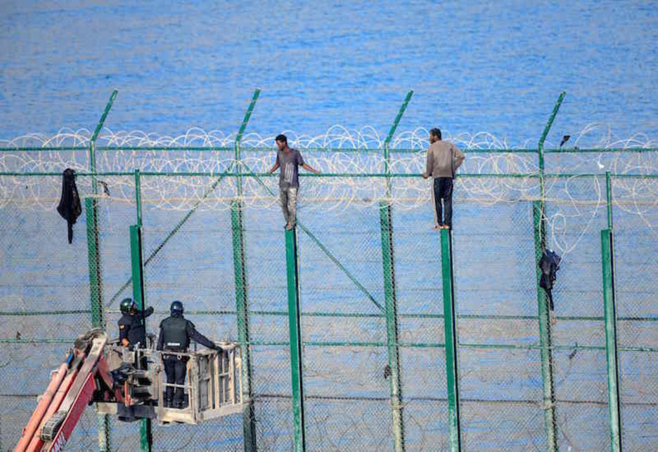 Efectivos de la Guardia Civil vigilan a dos migrantes subidos a la valla. (Antonio SEMPERE/AFP)