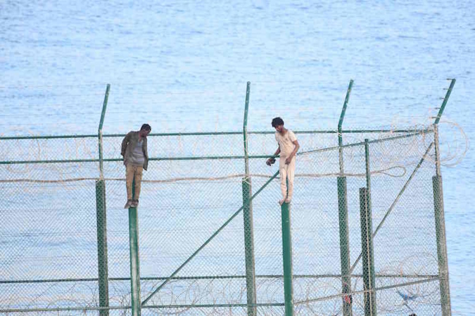 Dos migrantes encaramados en la valla fronteriza de Ceuta. (Antonio SEMPERE/AFP)