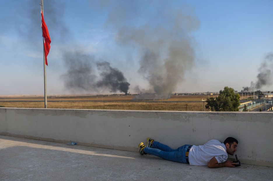 Un periodista se pone a cubierto mientras Turquía ataca la ciudad fronteriza del Tell Abiad. (BULENT KILIC  / AFP)