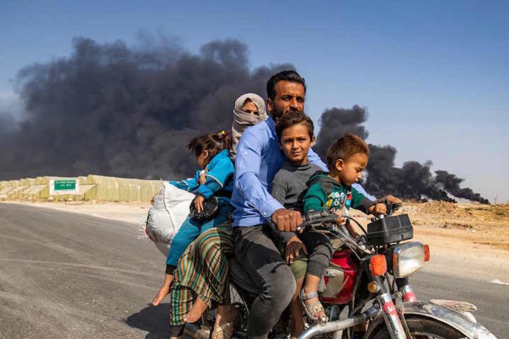 Una familia kurda huye en moto de Serekaniye, donde los kurdos provocan humaredas para obstaculizar los bombardeos turcos. (Delil SOULEIMAN/AFP)